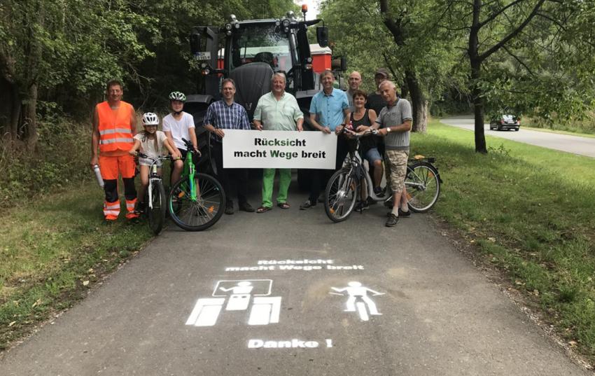 Mit Sprühkreide oder Sprühfarbe und einer Schablone werden der Appell „Rücksicht macht Wege breit“ und symbolisch ein Traktor und ein Radfahrer auf Feld- und Wirtschaftswegen aufgebracht, wie hier 2023 in Eberstedt im Weimarer Land. 